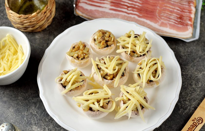 1. Этап. Шампиньоны в беконе в духовке: Выложите в каждую шляпку немного начинки, присыпьте тертым твердым сыром.