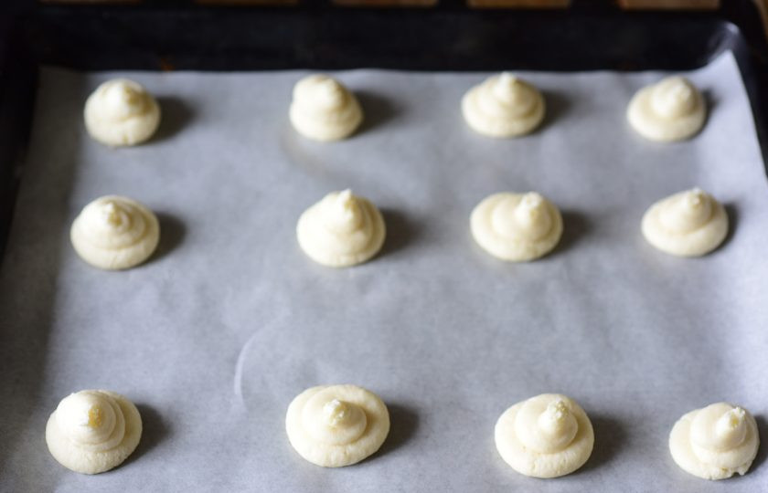 1. Этап. Кето-печенье из кокосовой муки: У кондитерского мешка с тестом отрежьте кончик и отсадите на противень, застеленный пергаментом, небольшие порции, формируя заготовки печенья.