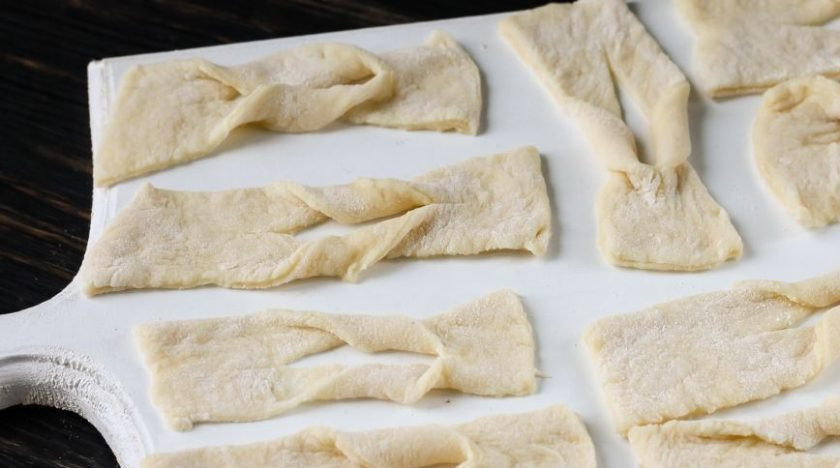 1. Этап. Хворост простой: Раскатайте тесто в тонкий пласт. Разрежьте его на прямоугольные кусочки, сделайте в центре каждого надрез. Заверните одну сторону каждого прямоугольника вовнутрь.