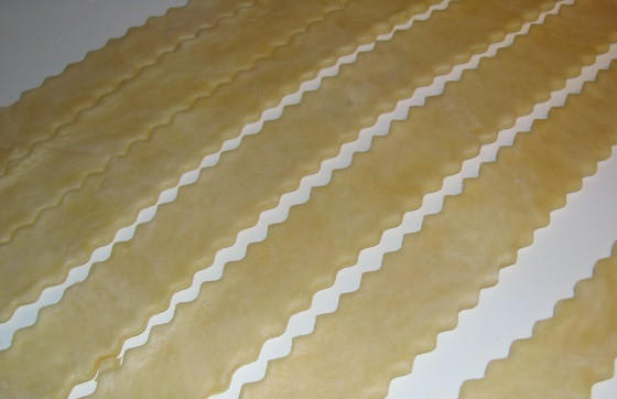 1. Этап. Турецкая самса: 7. Тесто выложите на присыпанную мукой поверхность и раскатайте довольно тонко. Нарежьте длинными полосками средней ширины. Чтобы турецкая самса в домашних условиях смотрелась более красиво, можно нарезать тесто при помощи фигурного ножа.