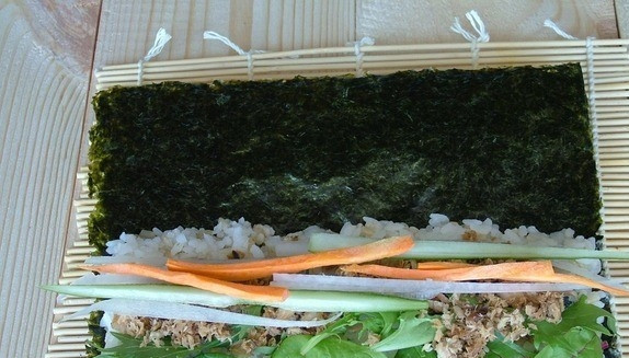 1. Этап. Роллы с тунцом консервированным: 3. Возьмите лист нори. Положите его на бамбуковый коврик. Выложите сверху все ингредиенты: сначала распределите рис. Поверх риса уложите листья салата, тунец и нарезанные овощи. Оставьте свободное место, чтобы была возможность завернуть.