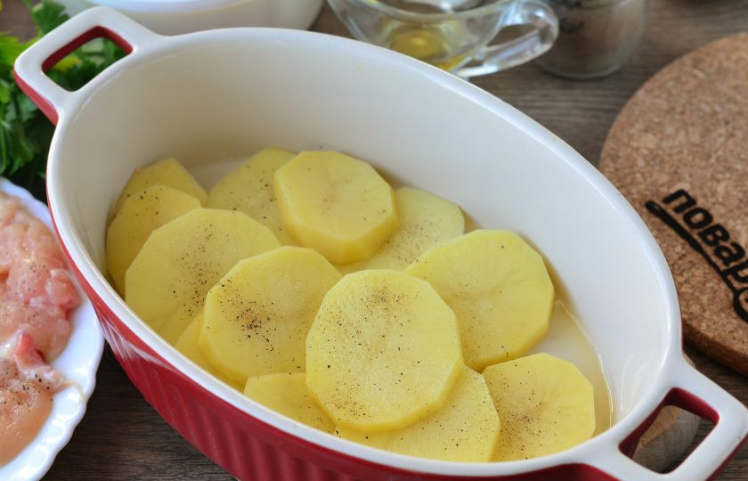 1. Этап. Курица в яично-сырной заливке: Картофель почистите и нарежьте кружочками, не сильно толстыми. Форму для запекания смажьте маслом, выложите картошку первым слоем. Посолите и поперчите по вкусу.