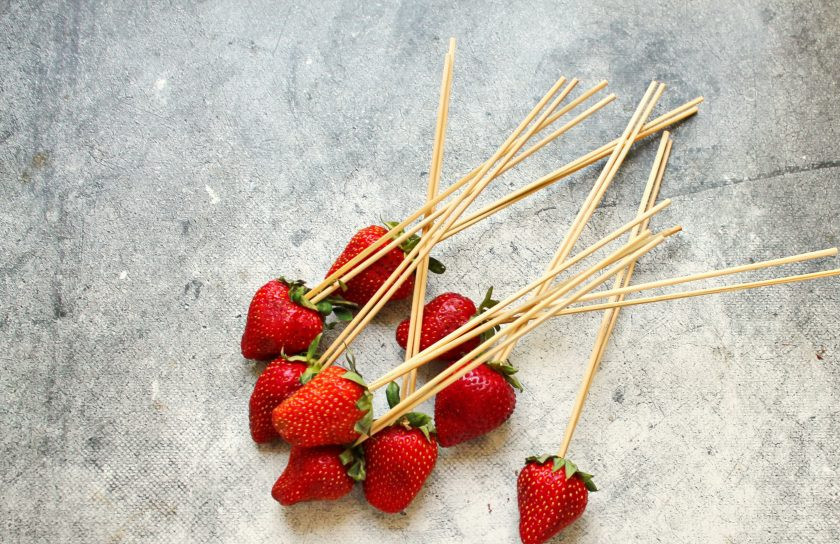 1. Этап. Летний торт: Каждую клубнику проткните двумя деревянными шпажками со стороны плодоножки, чтобы они плотно держали ягоду. Если шпажки толстые, можно взять одну.