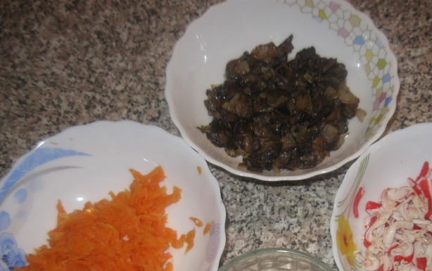 1. Этап. Салат с жареными крабовыми палочками и грибами: Морковь заранее отварите. Затем остудите её, почистите и натрите на крупной тёрке. В майонез выдавите чеснок.