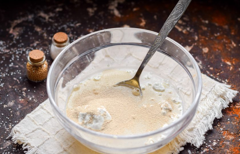 1. Этап. Оладьи без кефира и яиц: Влейте в миску воду, добавьте две ложки муки и ложку сахара. Всыпьте дрожжи, все перемешайте и уберите в тепло на 15 минут.