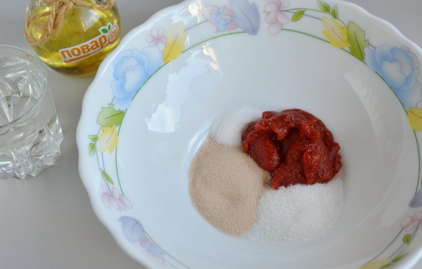 1. Этап. Томатные булочки: 2. В глубокой посудине соедините сахар, соль, дрожжи, пасту. Влейте теплую воду и перемешайте все до растворения.