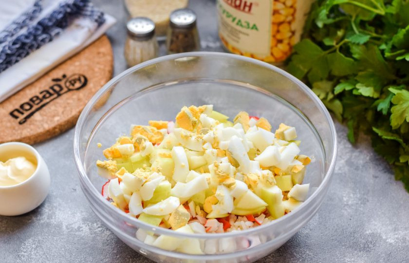 1. Этап. Крабовый салат с рисом и яблоком: Куриные яйца почистите и нарежьте небольшими кубиками, добавьте в салат.