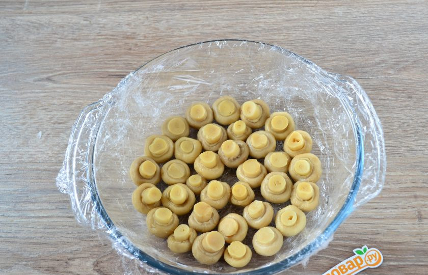 1. Этап. Салат Грибная поляна: Большую миску с плоским дном (или кастрюлю) застелите пищевой пленкой – так будет удобнее переворачивать салат. На дно выложите маринованные шампиньоны шляпками вниз.