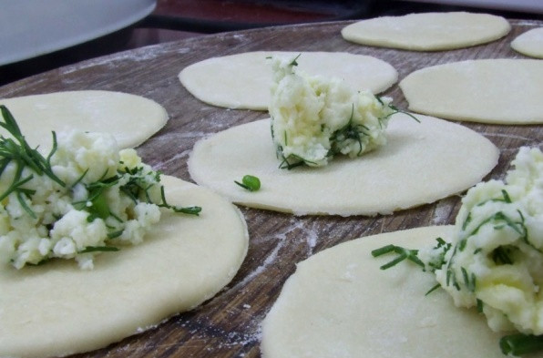 1. Этап. Вареники на кефире с творогом: В отдельной миске смешиваем кефир с содой и солью, в эту смесь подсыпаем частями муку и замешиваем тесто, одно должно получиться мягким, податливым и эластичным. Посыпаем стол мукой и раскатываем на нем тесто в тонкий пласт, вырезаем из теста кружочки. На каждый кружочек выкладываем нашу начинку из творога.
