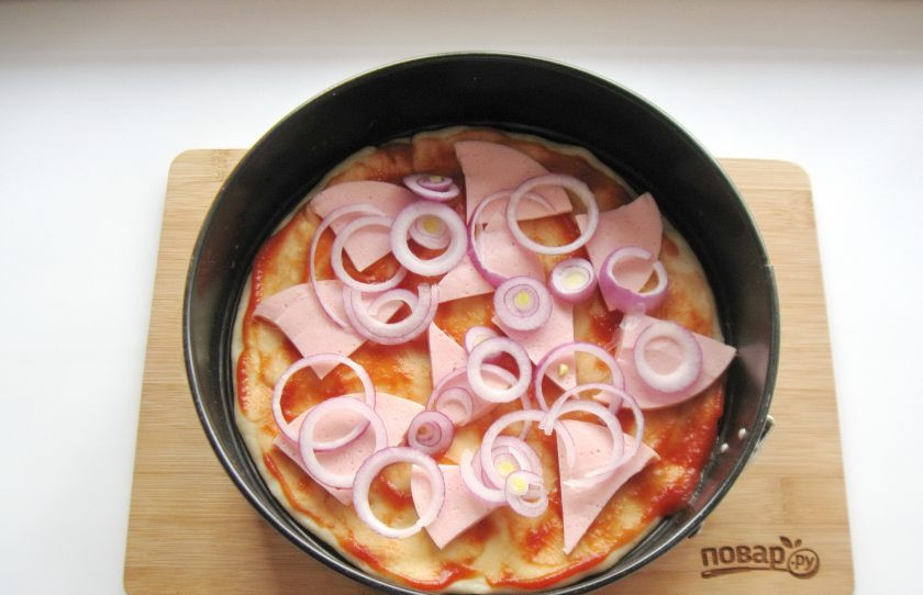 1. Этап. Самая вкусная пицца: Лук очистите, помойте и нарежьте кольцами. Выложите на колбасу.