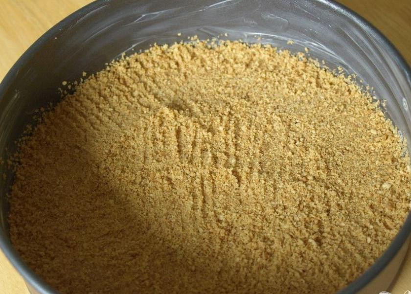 1. Этап. Чизкейк с малиной и шоколадом: 1. Разогреть духовку до 180 градусов. Растопить масло на медленном огне. Сыр достать из холодильника и выложить в тарелку. Оставить его на 15 минут при комнатной температуре. Растопить шоколад на водяной бане. Раздробить печенье. Смазать форму для выпечки сливочным маслом. Крошку из печенья выложить на дно миски и влить топленое масло. Тщательно перемешать вилкой. Высыпать смесь в форму для выпечки и равномерно распределить по дну. Спрессовать крошки сначала вилкой, а потом руками. Поставить в разогретую духовку на 20 минут и дать остыть.