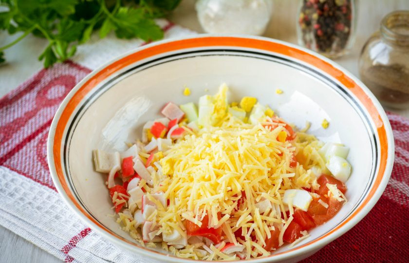1. Этап. Салат с крабовыми палочками и чипсами: Нарезанные компоненты сложите в глубокую миску, добавьте тертый сыр.