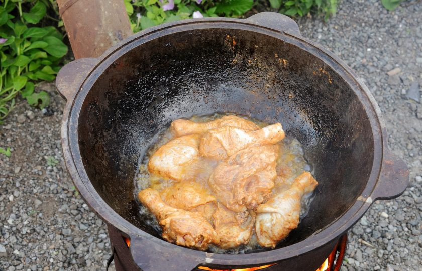 1. Этап. Куриные окорочка в казане на костре: Установите казан. Влейте растительное масло и хорошо его разогрейте на сильном огне. Шумовкой обдайте края казана раскалённым маслом. Осторожно, не обожгитесь! Отправьте курицу в казан.