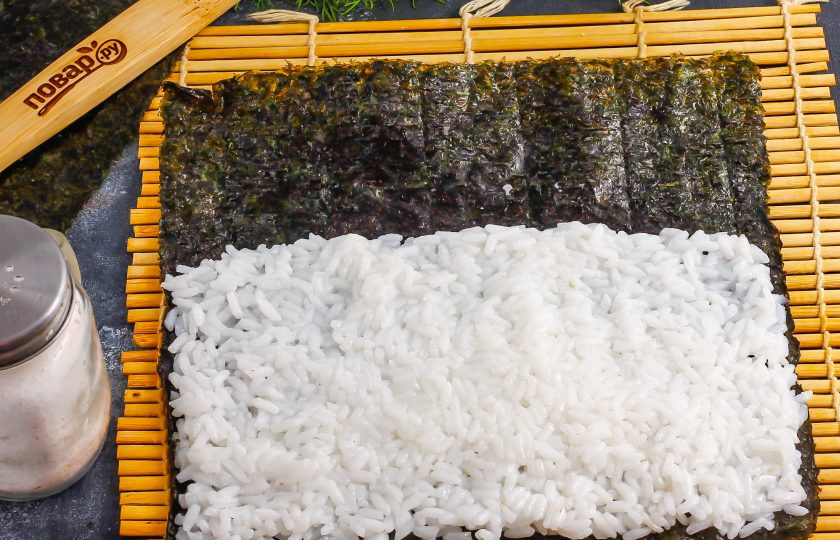 1. Этап. Темпура роллы: Расстелите коврик, а на него выложите лист нори. Смочите руки в воде и выложите на нори отварной рис, стараясь не заполнять водоросли с одного края на 2-3 см.