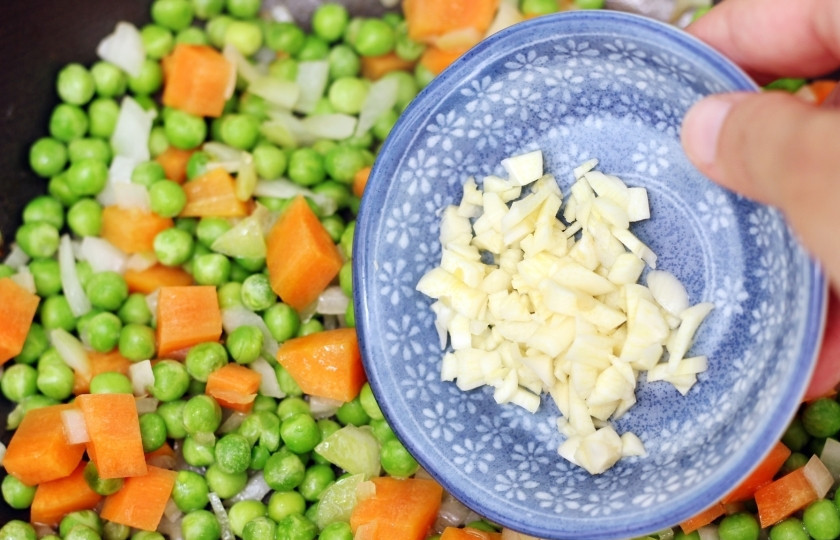 1. Этап. Жареный рис с курицей: Морковь нарежьте кубиками, небольшими. Смешайте с зелёным горошком и добавьте чеснок и лук. перемешайте овощи.