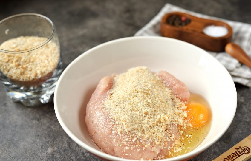 1. Этап. Куриные наггетсы без масла: Переложите фарш в глубокую миску, добавьте половину сухарей, соль и перец по вкусу. Хорошенько все перемешайте.