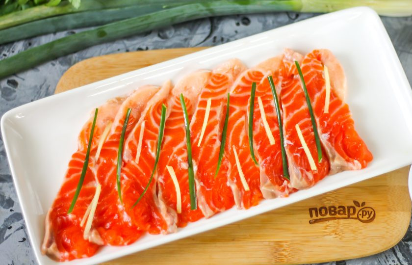 1. Этап. Сашими из лосося: Промойте зеленый лук, корень имбиря очистите от кожуры. Нарежьте и тот, и другой продукт тонкими полосками и выложите на рыбное филе.