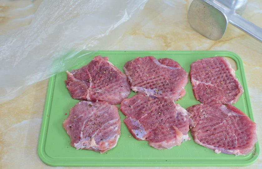 1. Этап. Свиные отбивные в картофельном кляре на сковороде: Свинину нарежьте на порционные кусочки и немного отбейте кухонным молоточком. При отбивании накрывайте мясо пленкой, чтобы не летели брызги и края кусочков не рвались. Посыпьте мясо солью и специями.