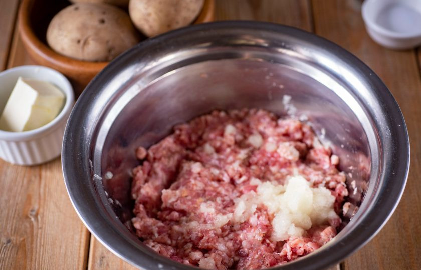 1. Этап. Картофель, фаршированный с рисом: Фарш выложите в миску, добавьте соль, перец черный, натрите на мелкую терку очищенный лук. Перемешайте все ложкой.