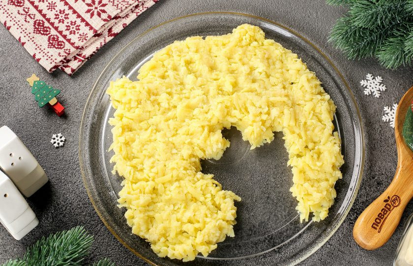 1. Этап. Селедка под шубой на год Дракона: Картофель натрите на крупной терке и выложите первым слоем в виде будущего дракона. Тарелка должна быть плоской и достаточно большой. Картофель посолите и смажьте майонезом.