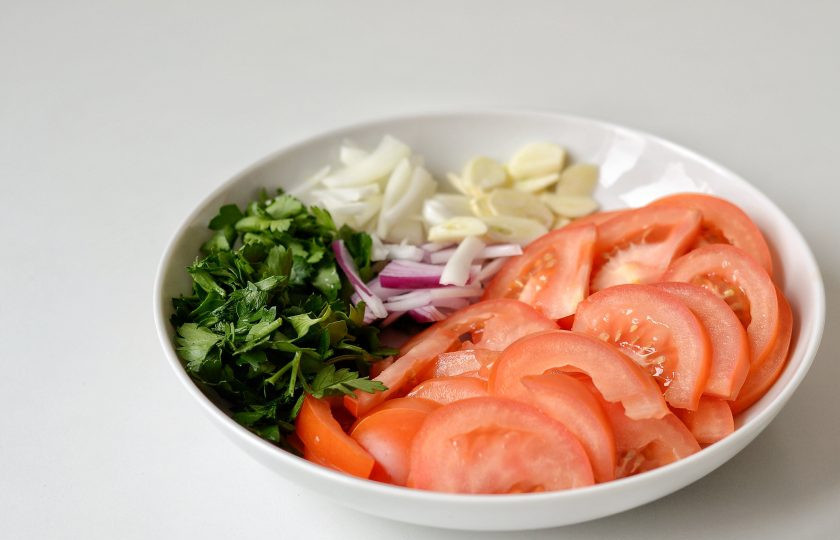 1. Этап. Салат из красных помидоров на зиму: Помидоры нарежьте на ломтики среднего размера. Плодоножку удалите. Лук нарежьте тонкими полукольцами. Петрушку мелко нашинкуйте, чеснок нарежьте тонкими дольками.