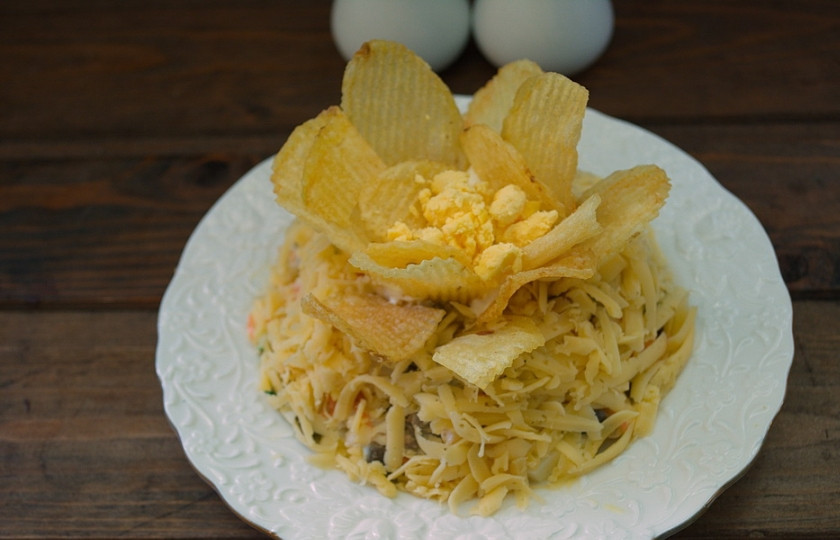 1. Этап. Салат Орхидея с курицей: Выберите чипсы двух видов: более широкие и большие и более мелкие. Из мелких создайте внутренние чашу лепестков орхидеи, а более крупными декорируйте края. Получим цветов из 2 или нескольких чашелистиков. Натрите на терке желток яичный. Посыпьте им центр цветка.