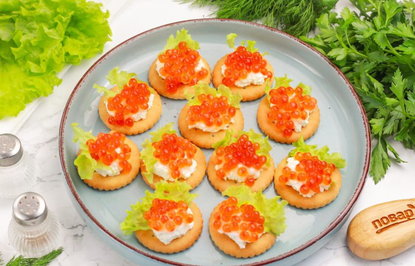 1. Этап. Канапе на крекерах на праздничный стол: Затем сверху выложите красную икру. Можно заменить ее черной икрой, имитированной икрой лосося или икрой мойвы.