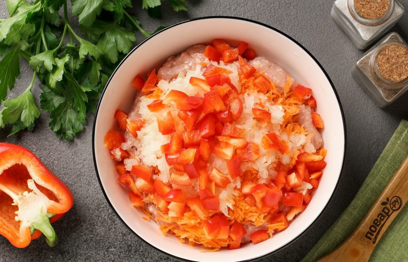 1. Этап. Куриные котлеты с овощами: Переложите фарш в глубокую миску. Добавьте натёртую на мелкой тёрке морковь. Лук натрите на крупной тёрке, а болгарский перец нарежьте небольшими кубиками.