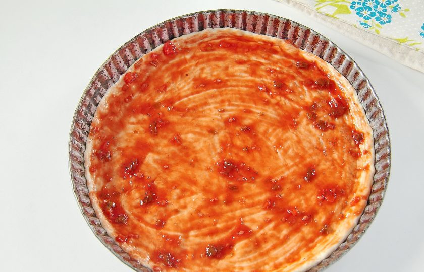 1. Этап. Простая пицца с луком: 8. Тесто разделите на две части. Раскатайте тонко на присыпанной мукой поверхности и аккуратно перенесите в форму для выпечки, смазанную маслом. Сформируйте руками небольшие бортики и смажьте тесто кетчупом или любым томатным соусом.