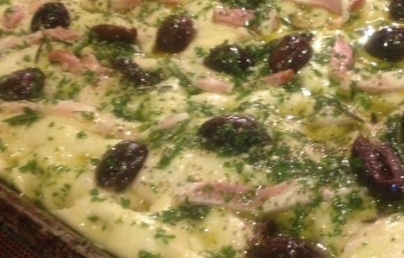 1. Этап. Фокачча с оливками и беконом: 4. Когда тесто увеличилось в 2 раза, выложите его на смазанный противень и вручную растяните его по всему противню. Пальцем сделайте углубления, добавьте поверх теста оливки, кусочки бекона, зелень, оставшееся оливковое масло, цедру, измельченный чеснок и посолите. Оставьте на 1 час.