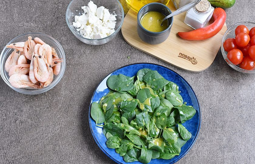 1. Этап. Салат с креветками, авокадо и помидорами черри: На сервировочные тарелки выложите промытый и просушенный шпинат. Сбрызните частью заправки.