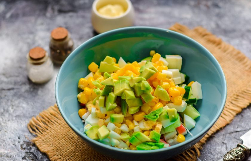 1. Этап. Салат с кукурузой, авокадо и крабовыми палочками: Добавьте в салат кукурузу и нарезанный кубиками авокадо.