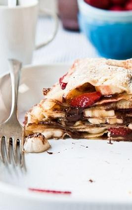 1. Этап. Блинный торт с клубникой: 3. На противень застелите пергамент. Положите на лист два блина. Намажьте верхний блин шоколадной пастой и положите немного клубники и бананов. Закройте ягоды третьим блинов и повторите процедуру. Таким образом, выкладывайте все блины, смазывайте их шоколадной пастой и кладите сверху ягоды. Духовку разогрейте чуть-чуть. Поставьте торт в духовку ненадолго, чтобы он прогрелся. Все, торт готов. Обсыпьте его сверху сахарной пудрой и можно пробовать. Нет, не пробовать, а есть. Потому что он получился очень вкусный.