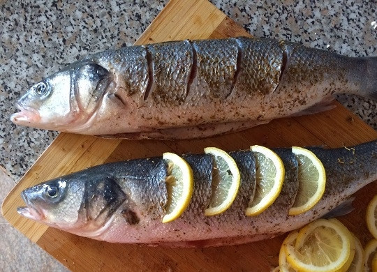 1. Этап. Сибас запеченный: 2. Посолите сибаса, добавьте по вкусу перец или специи для рыбы. Сделайте небольшие надрезы и разместите в них ломтики лимона. Остальной лимон вместе с луком поместите в брюшко.