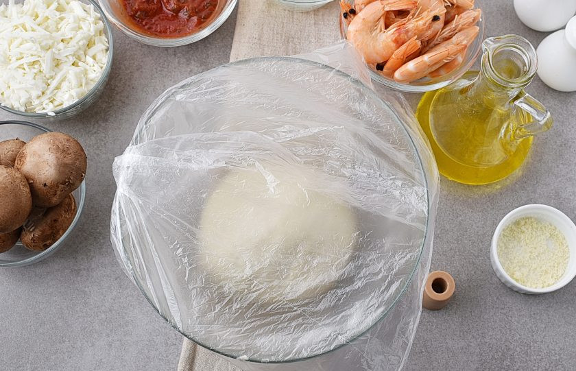 1. Этап. Пицца с креветками и грибами: Вымешанное тесто слегка смажьте маслом, верните в миску и накройте пленкой. Уберите в теплое место на час.