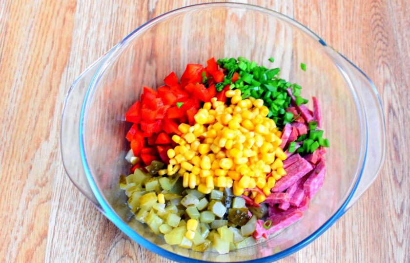 1. Этап. Блинный салат с колбасой: Нарежьте колбасу нетолстыми брусочками. Огурцы и перец нарежьте кубиками. Измельчите лук и обсушите консервированную кукурузу. Смешайте все в просторной миске.