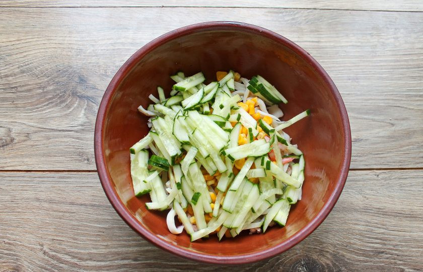 1. Этап. Салат с кальмарами, креветками и кукурузой: Огурец порежьте соломкой и добавьте в салат.