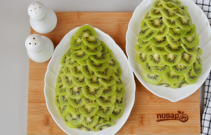 1. Этап. Салат Новогодний: Очистите киви, порежьте на половинки, потом каждую тонкими слайсами. Закройте слайсами весь салат.