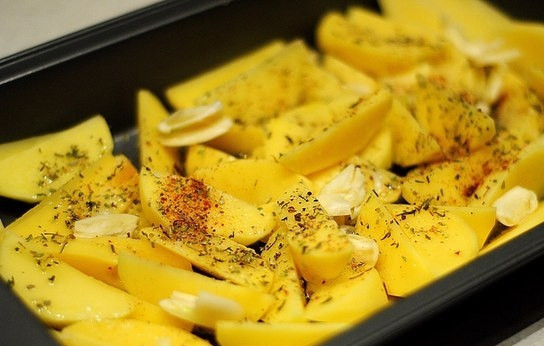 1. Этап. Маринованная в кефире курица с картофелем: На дно формы для запекания выкладываем некрупно нарезанный картофель и специи, поливаем оливковым маслом. Кладем в форму несколько раздавленных долек чеснока.