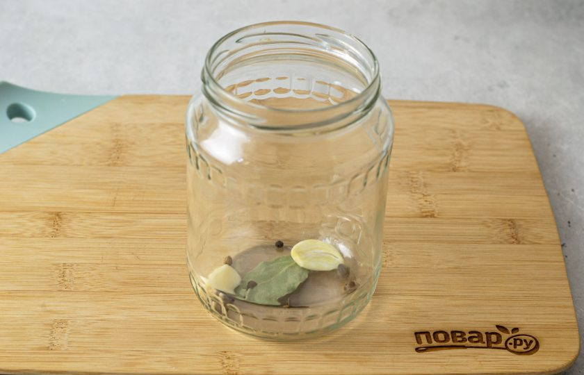 1. Этап. Консервированные огурцы с уксусом: На дно чистой стерилизованной банки выложите очищенный чеснок, перец горошком, гвоздику и лавровый лист.