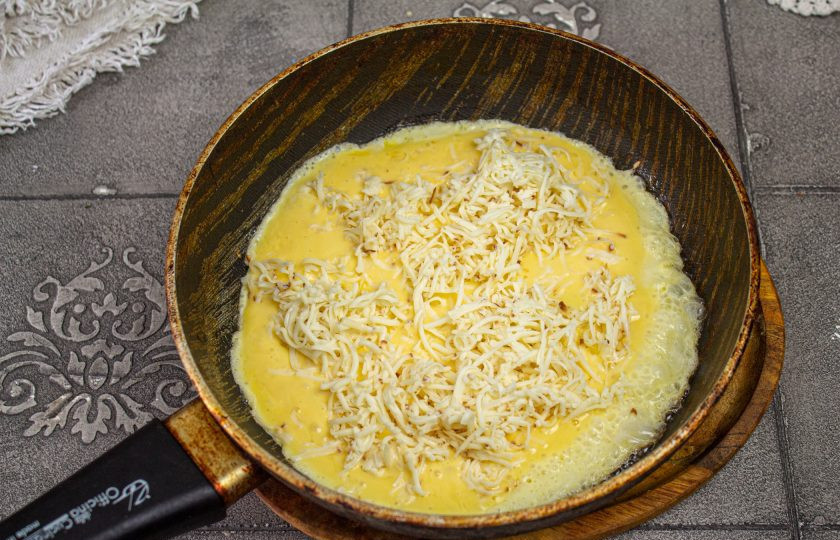 1. Этап. Трёхслойный торт-омлет: Сковороду нагрейте с 1 столовой ложкой масла, вылейте омлетную массу и сверху разложите натертый сыр. Готовьте под крышкой 4-5 минут при небольшом нагреве до готовности. Омлет переворачивать не нужно. Как полностью схватится сверху переложите на блюдо.