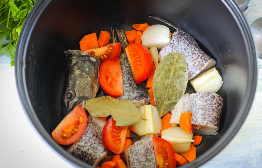 1. Этап. Уха из щуки в мультиварке: Промойте помидоры, вырежьте из них зеленые сердцевинки и нарежьте ломтиками. Выложите вместе с лавровыми листьями в емкость.