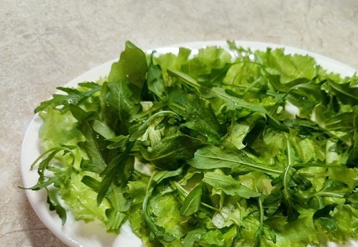 1. Этап. Салат с индейкой и авокадо: Собираем салат. На плоское блюдо уложить порванные листья салата и горсть рукколы. Или любой салатный микс. Полить частью заправки.