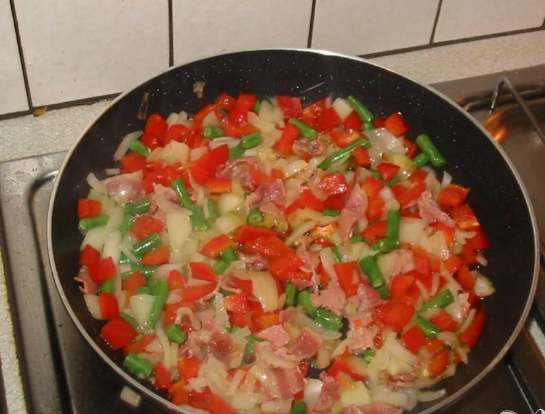 1. Этап. Традиционная испанская паэлья: 2. Разрезать болгарский перец на две части, вырезать серединку и семена, нарезать перец небольшими кусочками. Нагреть оливковое масло в сковородке на среднем огне, добавить бекон, лук и перец и жарить 8 минут, пока ингредиенты не размякнут.