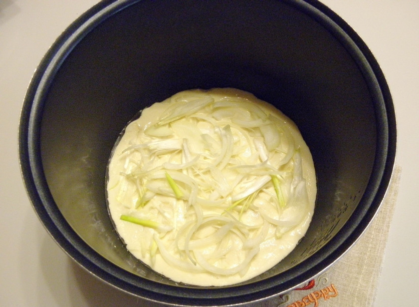 1. Этап. Заливной пирог с рыбными консервами: Возьмите антипригарную форму или кастрюлю мультиварки. Смажьте её растительным маслом, налейте половину теста. Распределите лук, отступив от края по 1 см.