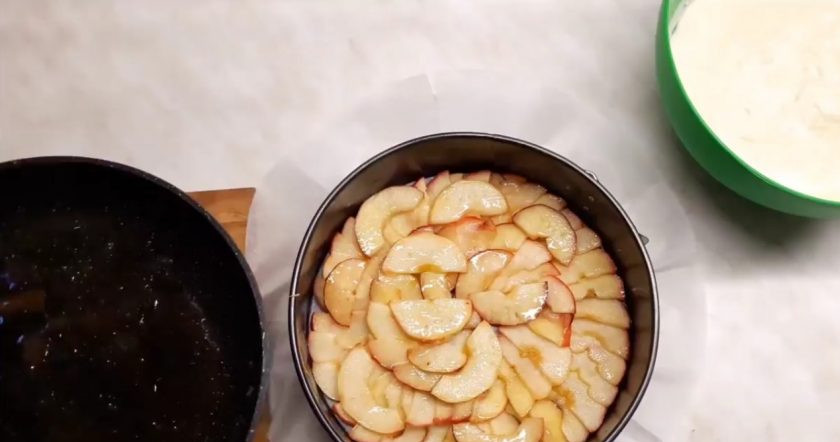 1. Этап. Пирог с яблоками по-Афински: 4. Выложите яблоки на застеленную пергаментной бумагой форму по всему дну. Залейте яблоки оставшимся яблочным сиропом со сковородки. Залейте яблоки тестом, немного разровняйте и накройте сверху пергаментной бумагой, чтобы пирог не подгорел.