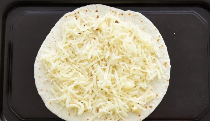 1. Этап. Пиццадилья: 2. Выложите тортилью на противень, посыпьте немного сыром.