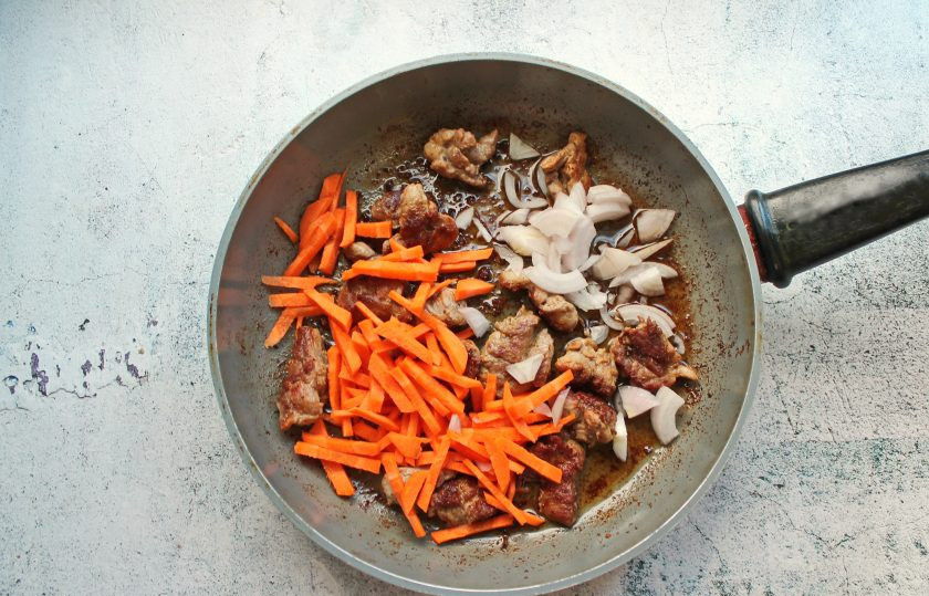 1. Этап. Плов с уткой и черносливом: Репчатый лук почистите и порежьте, добавьте к утке. Морковь почистите и нарежьте средней соломкой, выложите в сковороду. Обжаривайте в течение 10 минут на среднем огне, перемешивая.