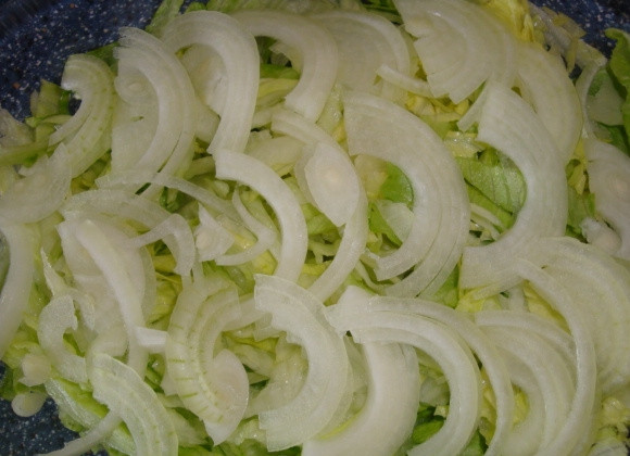 1. Этап. Cалат с фетой и оливками: Репчатый лук почистите, нарежьте полукольцами и выложите поверх салата Айсберг.