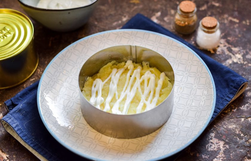 1. Этап. Мимоза с консервой: Подготовьте форму для салата. Картофель очистите и натрите средней стружкой. Уложите картофель первым слоем. Каждый слой салата смазывайте майонезом, солите и перчите.